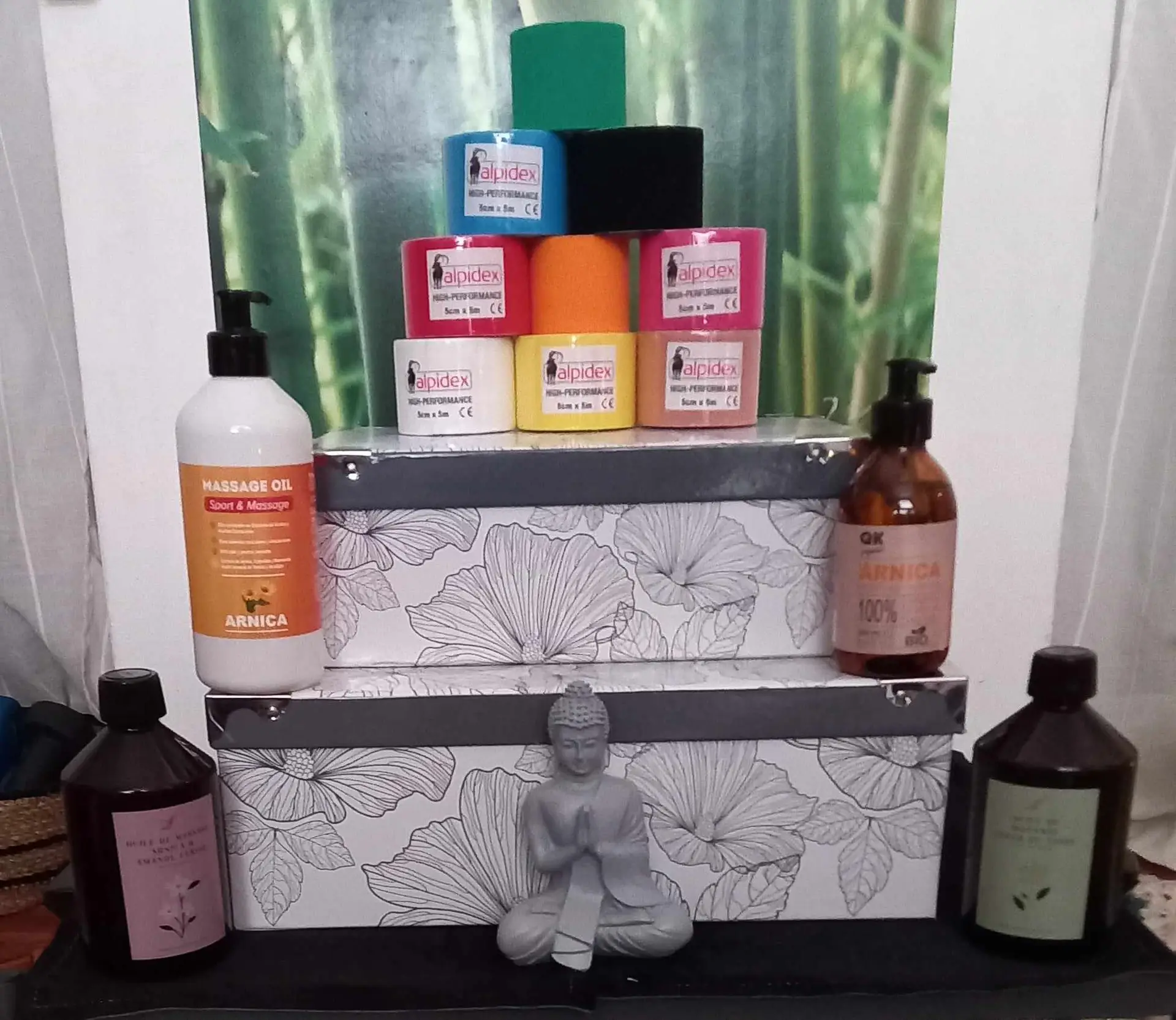 Huiles de massages, rouleaux de taping kinésiologiques de différentes couleurs, boudha, boites décoratives sur fond de décoration murale bambou